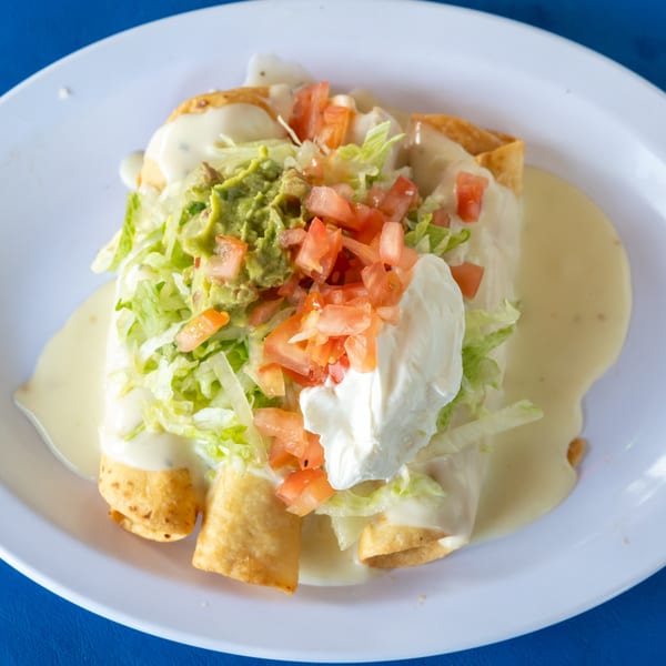 Crispy taquitos covered in white cheese sauce, shredded lettuce, guacamole, diced tomatoes, and sour cream.