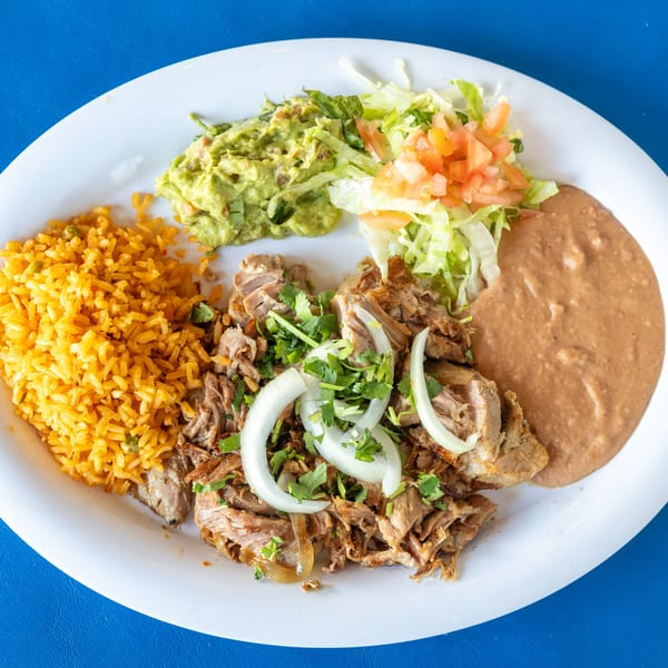 Carnitas plate with rice, refried beans, guacamole, and salad on a white plate.