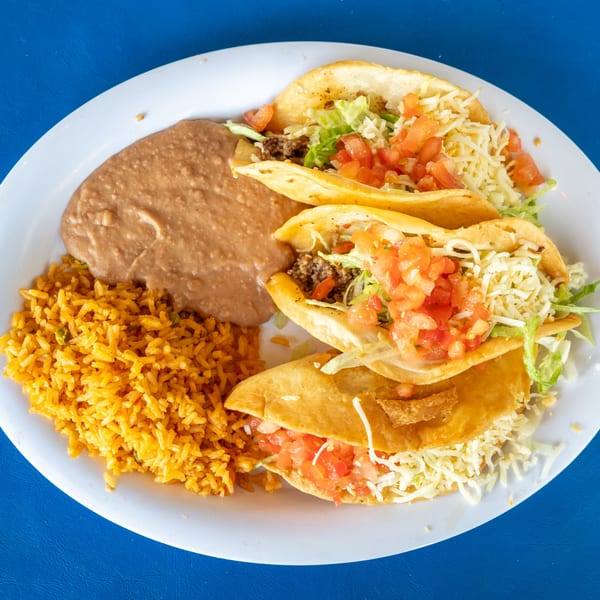 Three crispy tacos with ground beef, lettuce, cheese, and tomatoes, served with rice and refried beans.