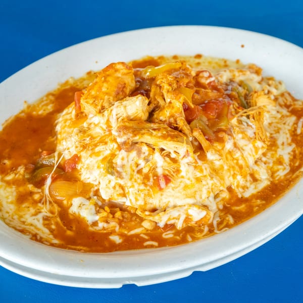 A white plate filled with chicken and vegetables in a rich orange sauce, topped with melted cheese.